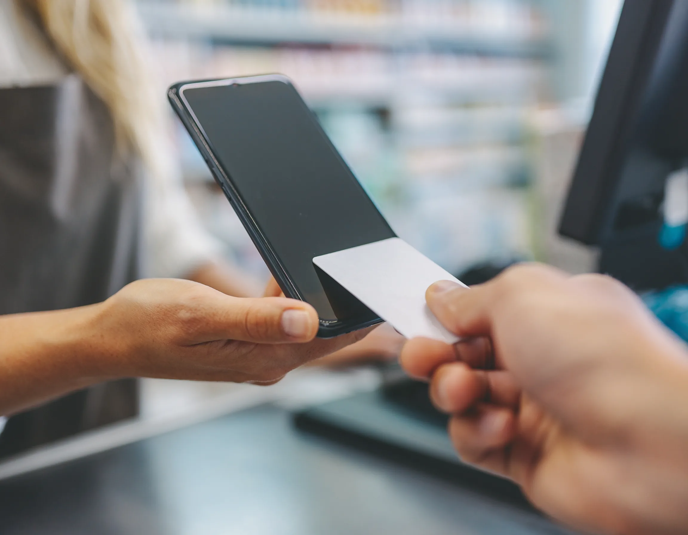 Customer presenting a contactless card to a merchant smartphone at checkout